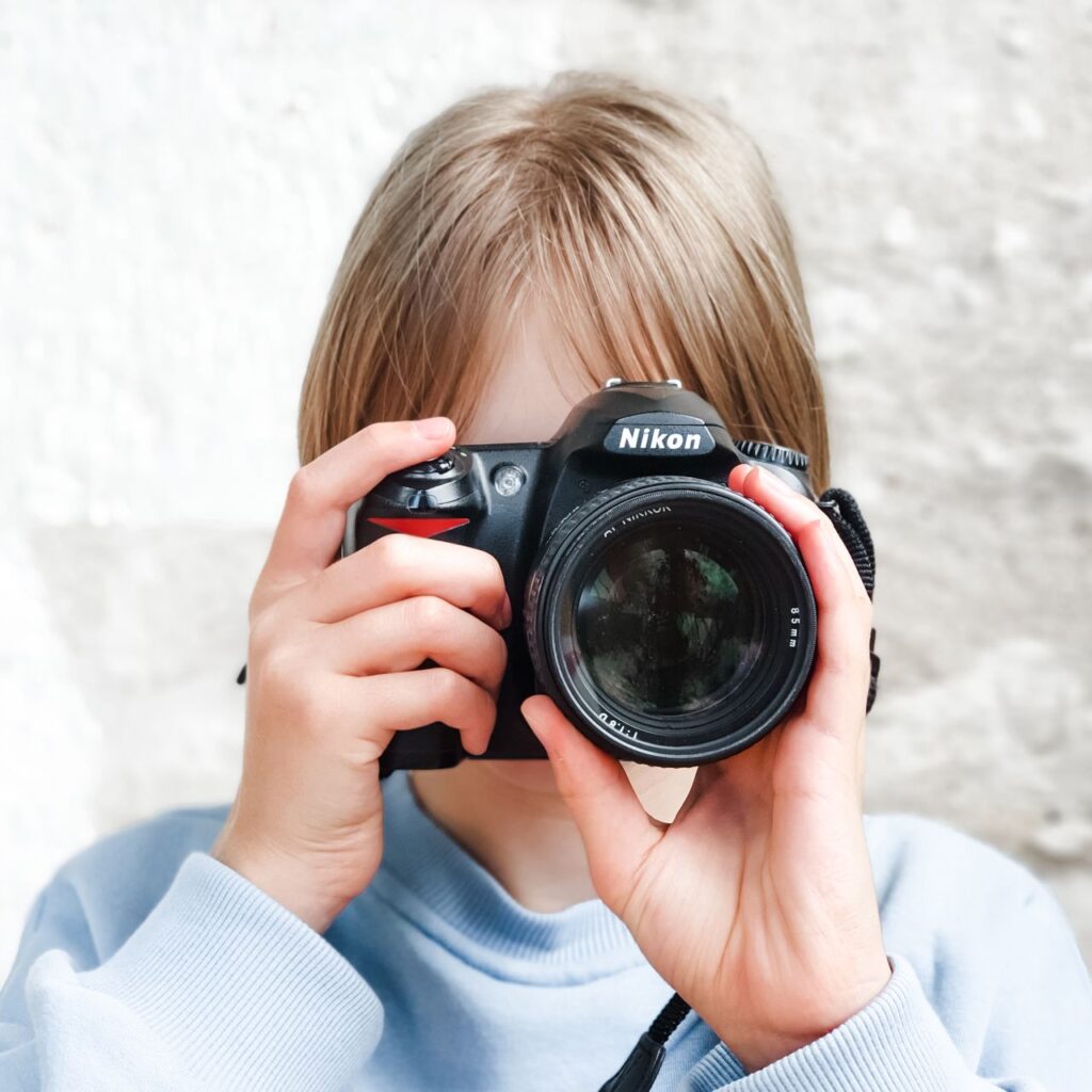 A young individual holding a DSLR camera, ready to capture moments indoors.