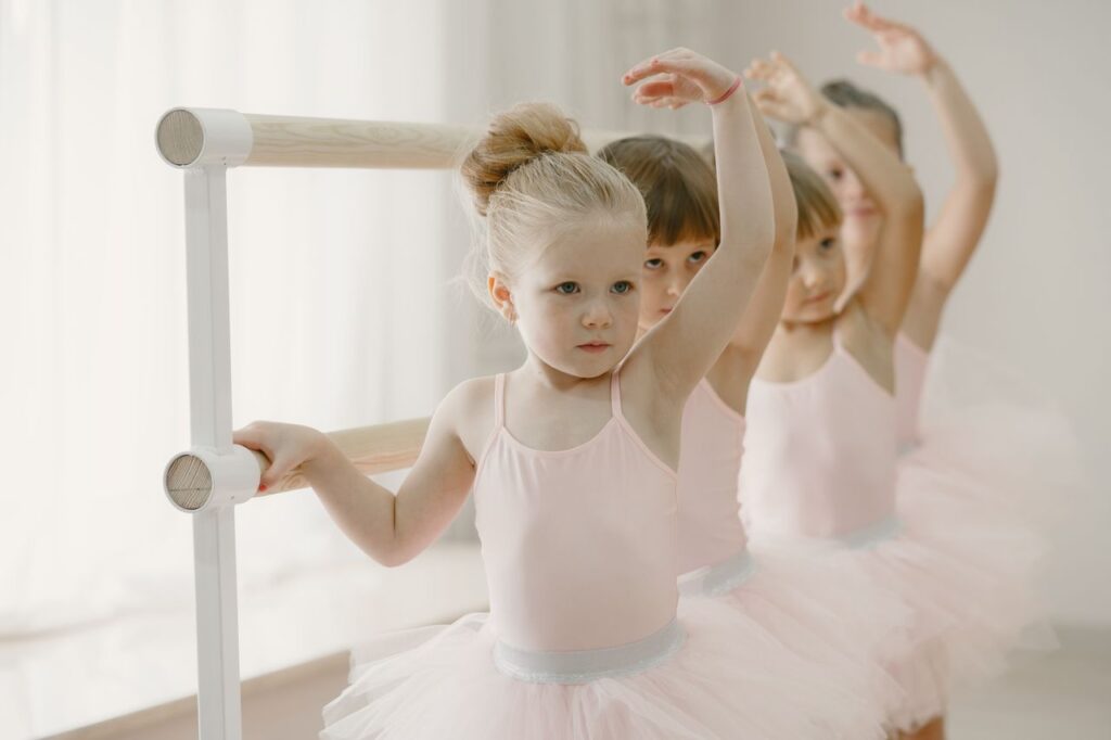Group of young girls in pink tutus practicing ballet indoors at a barre.