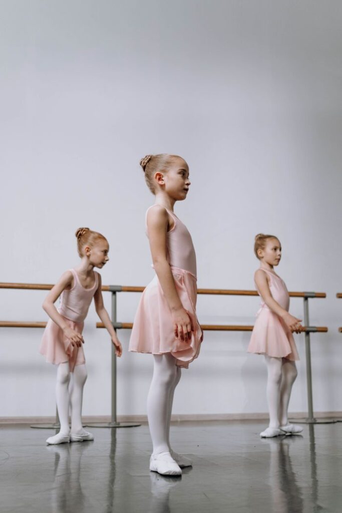Three young ballet dancers practice in a studio, wearing pink tutus and white tights.
